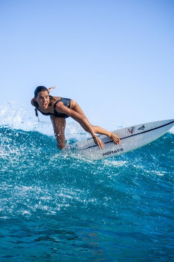 Surfeuse qui utilise une planche de surf nomads surfing sur une vague et un décor paradisiaque